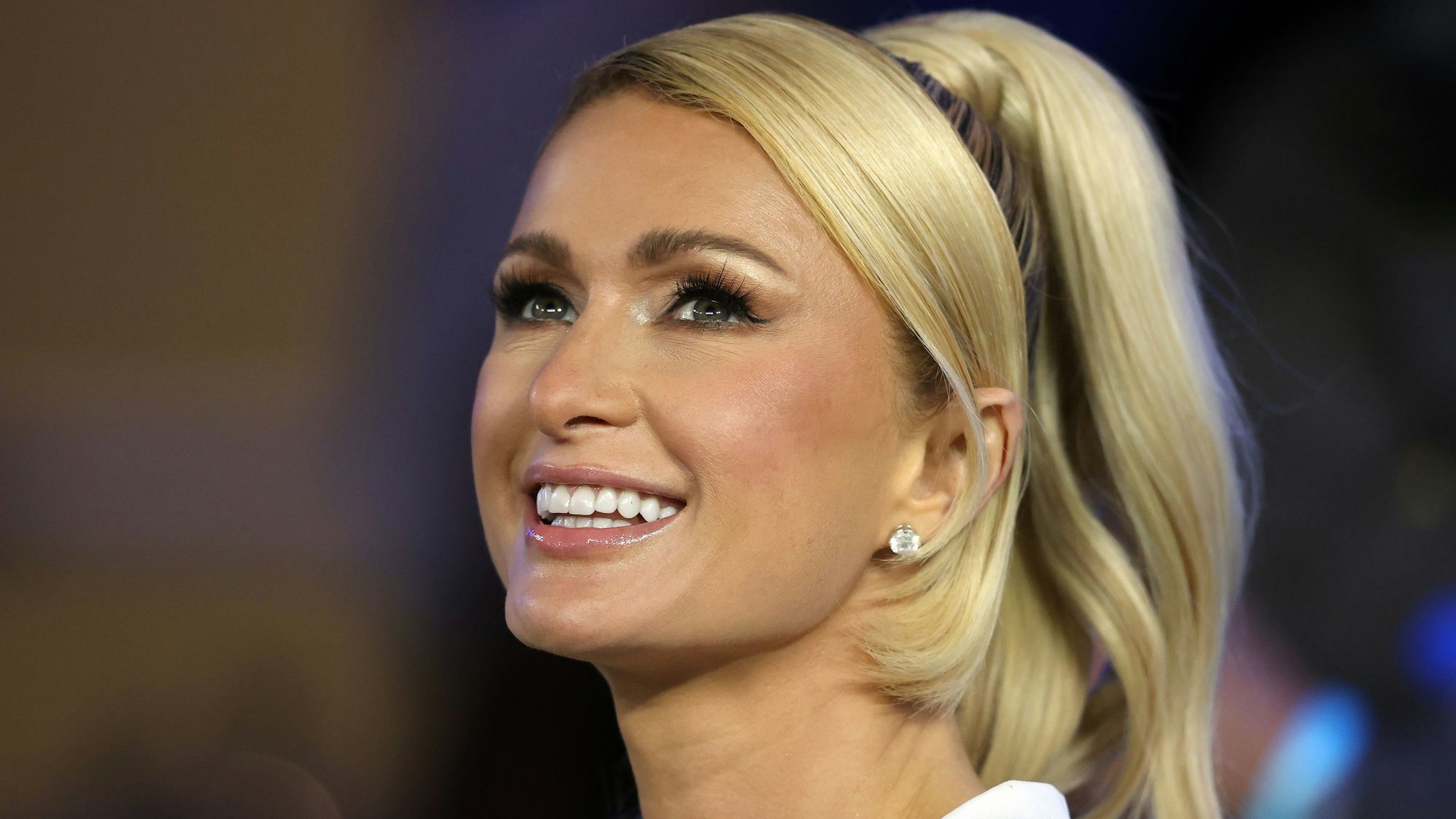 Paris Hilton lacht freundlich an der Kamera vorbei.