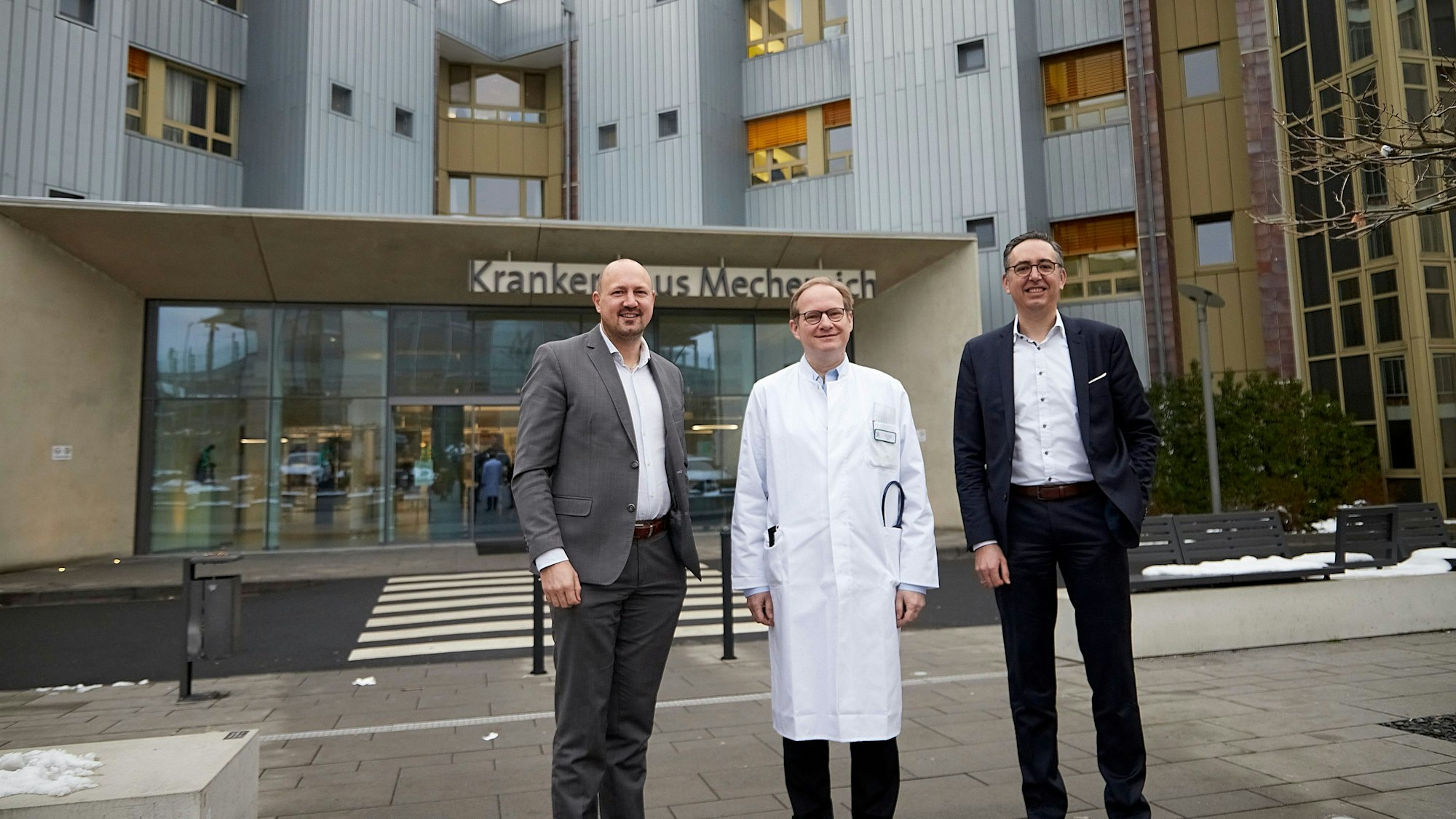 Drei Männer, der Mittlere im Arztkittel, stehen vor dem Eingang zum Kreiskrankenhaus Mechernich.