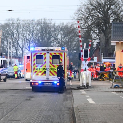 Rettungswagen und Polizeiautos stehen vor einem Bahnübergang.