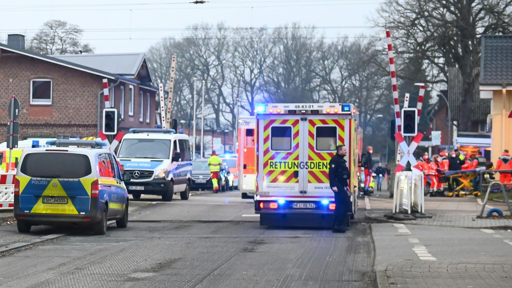 Rettungswagen und Polizeiautos stehen vor einem Bahnübergang.