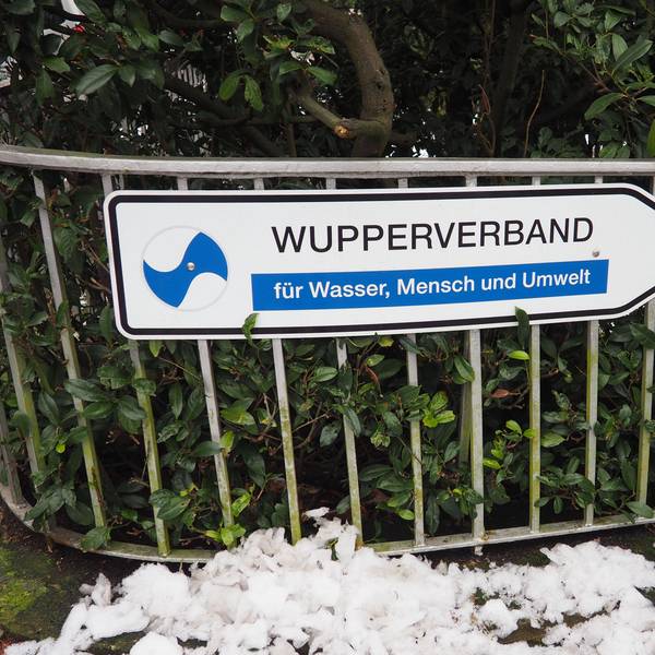 Ein Wegweiser mit der Aufschrift „Wupperverband für Wasser, Mensche und Umwelt“ vor einer grünen Hecke an einem Zaun vor der Verbandszentrale in Wuppertal.