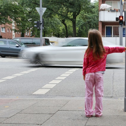 Eine Grundschülerin wartet an einer Rot zeigenden Ampel.