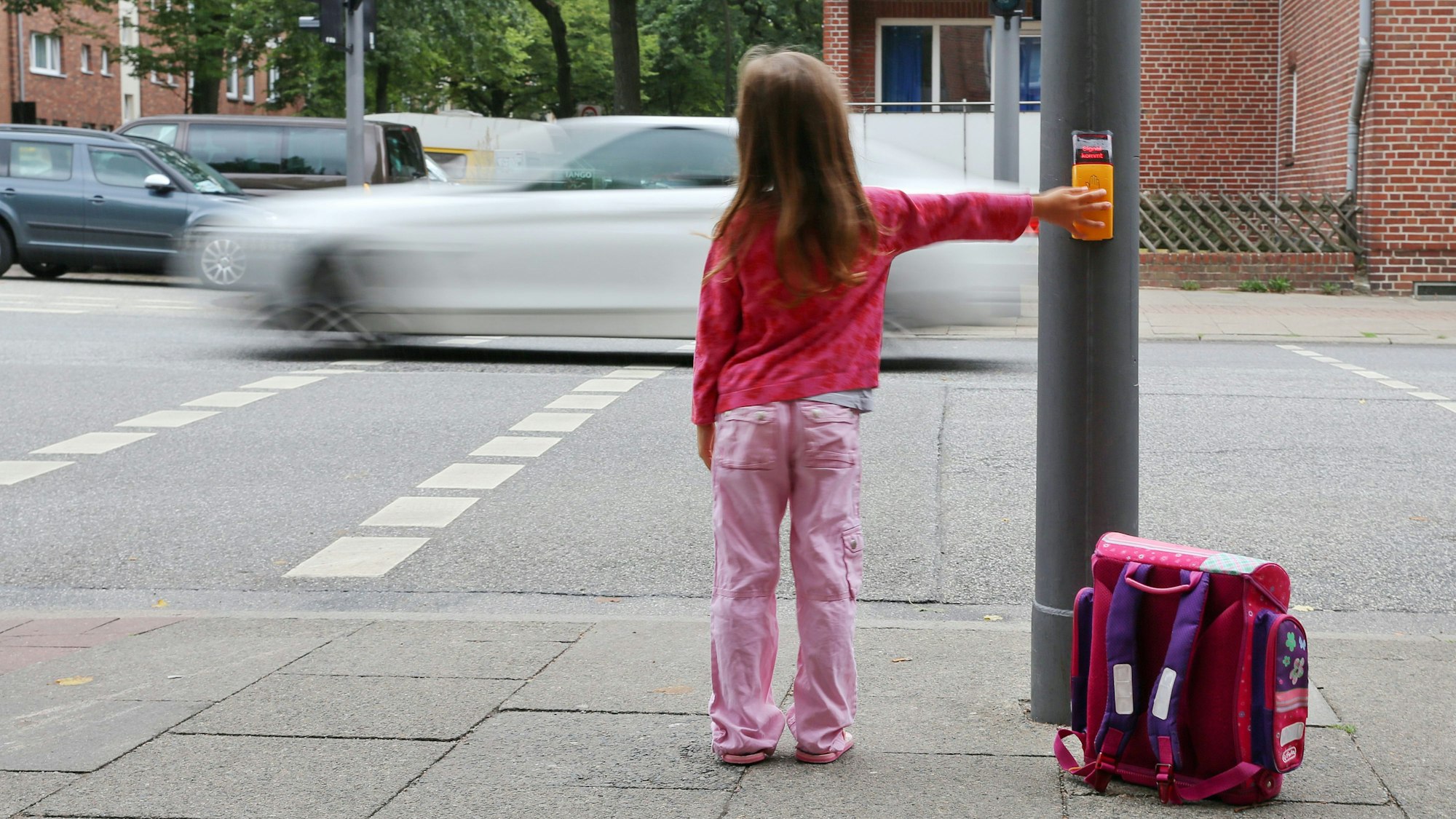 Eine Grundschülerin wartet an einer Rot zeigenden Ampel.
