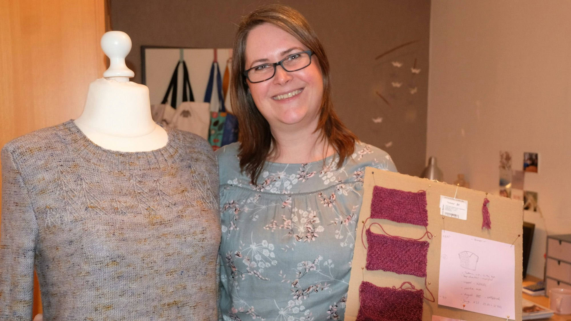 Frau mit einem Strickpullover an einer Schaufensterpuppe und Strickmustern