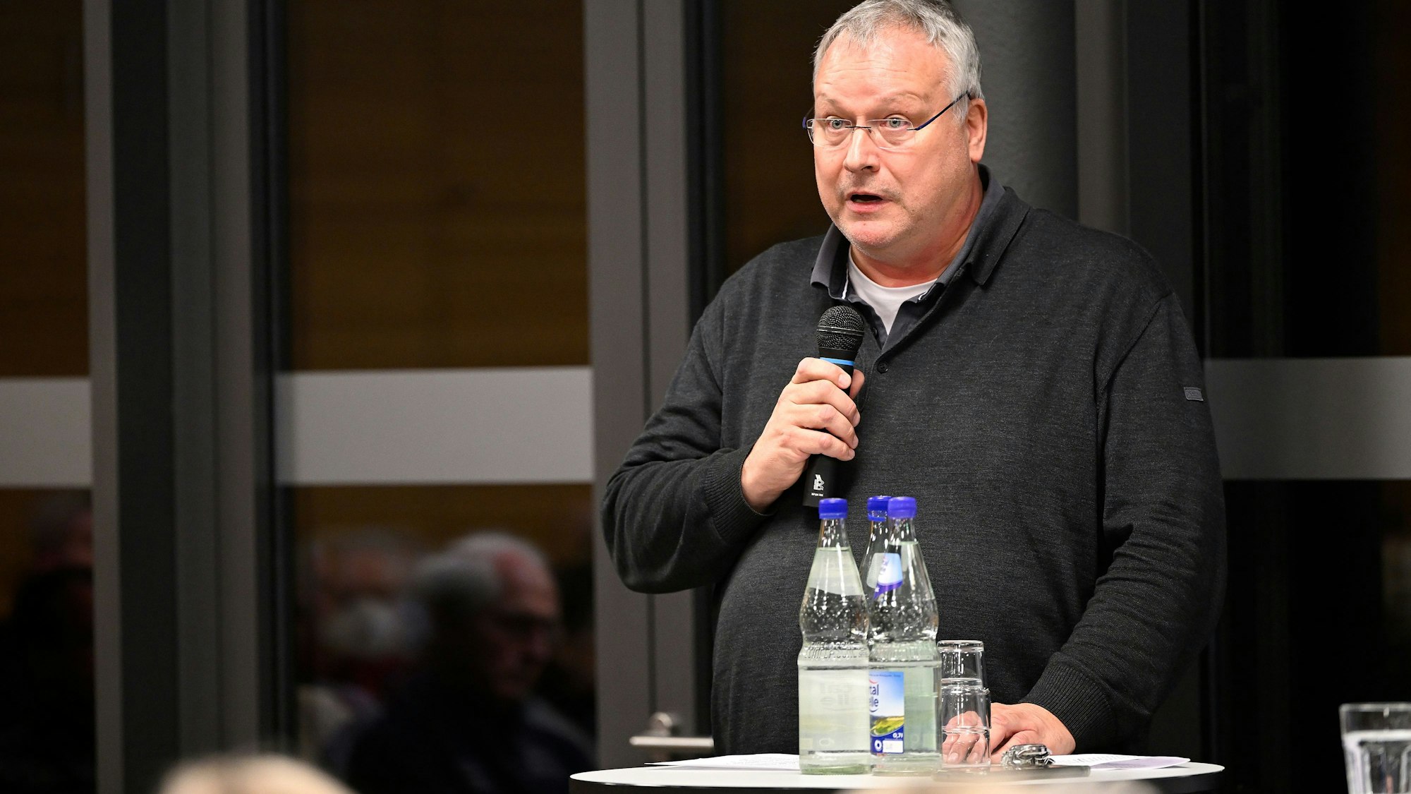 Der katholische Pfarrer Winfried Kissel steht mit einem mikrofon vor einem auditorium und spricht.