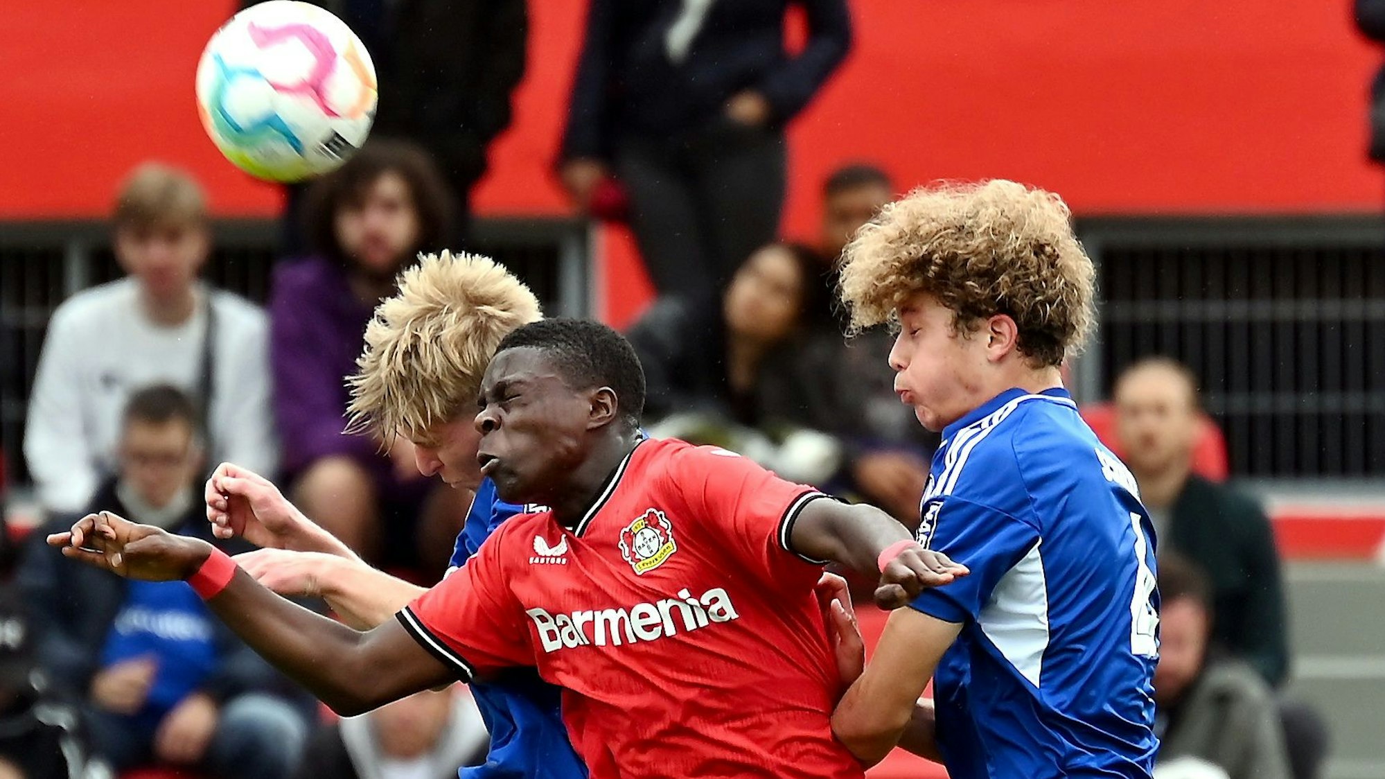 Ein Fußballer setzt sich gegen zwei Gegenspieler im Kopfball durch.