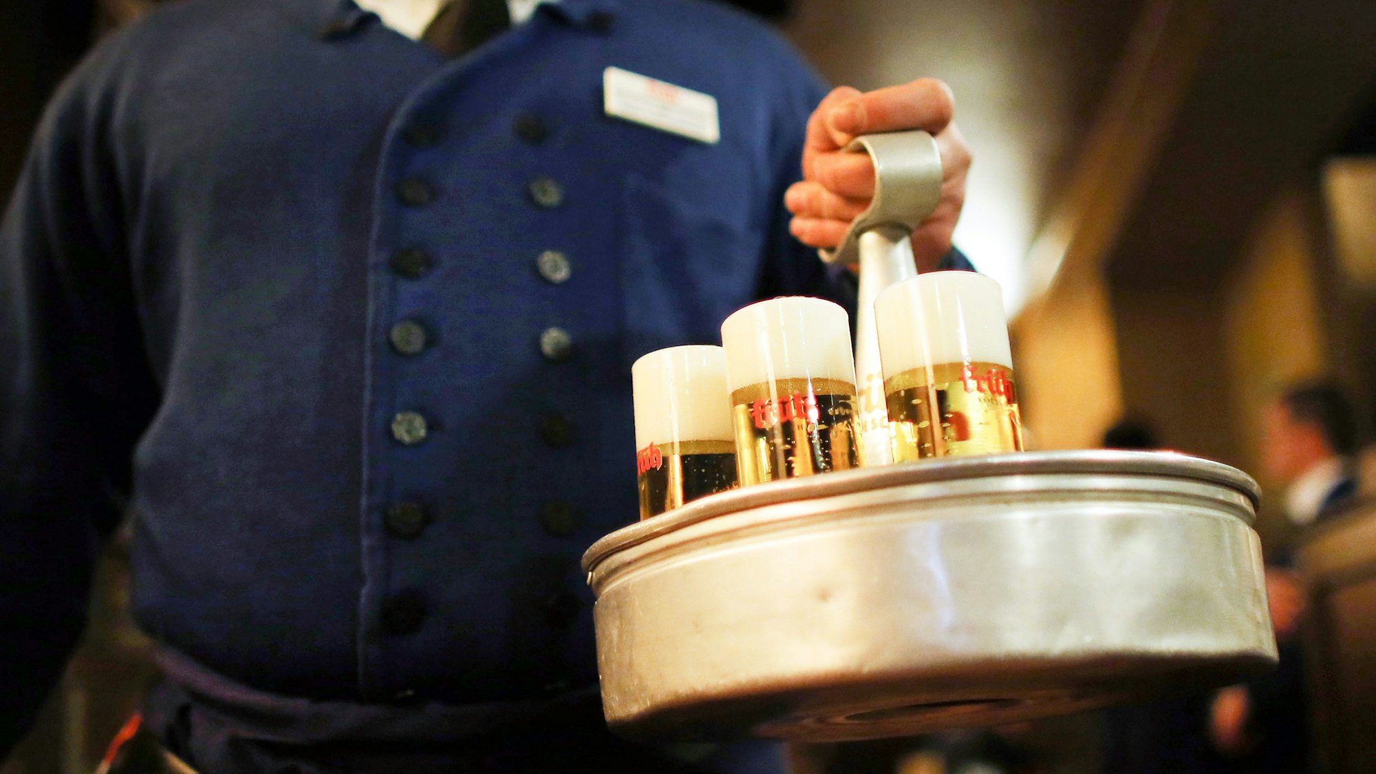 Ein Köbes (Kellner) trägt im Brauhaus Früh am Dom Kölsch-Bier. Das Oberlandesgericht Düsseldorf verhandelt über die Einsprüche von drei Kölsch-Brauereien gegen Bierkartell-Bußgelder der Kartellamtes. Das Bundeskartellamt hatte wegen verbotener Preisabsprachen im Rahmen des «Bierkartells» hohe Geldbußen gegen die Kölner Brauereien Früh, Gaffel und Erzquell verhängt. Dagegen haben die Brauereien Einspruch eingelegt. +++ dpa-Bildfunk +++