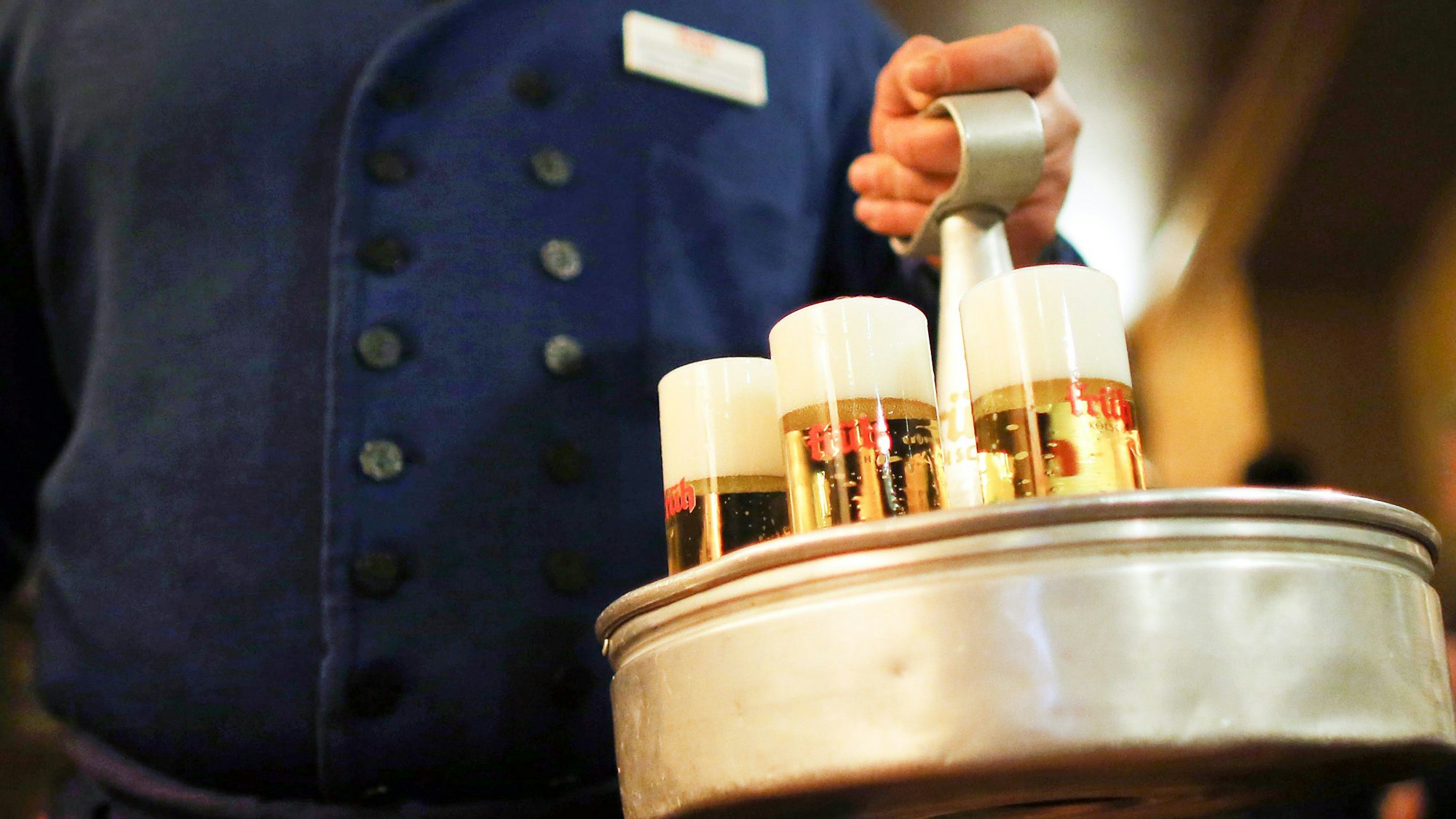 Zu sehen ist ein Köbes (Kellner), der im Brauhaus Früh am Dom Kölsch-Bier trägt.