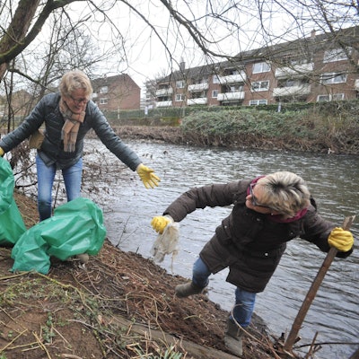 Drei freiwillige Helferinnen mit Müllsäcken am Wupperufer.