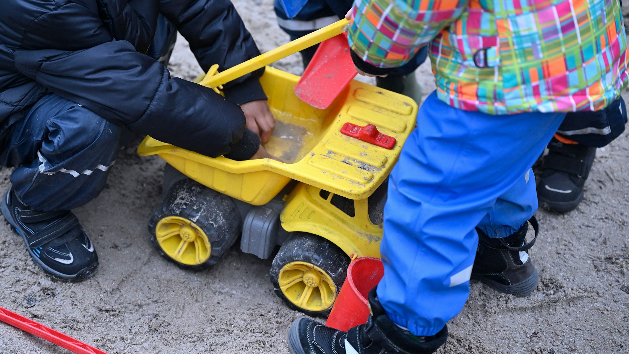 Spielende Kinder im Sandkasten mit einem großen, gelben Plastiklieferwagen.