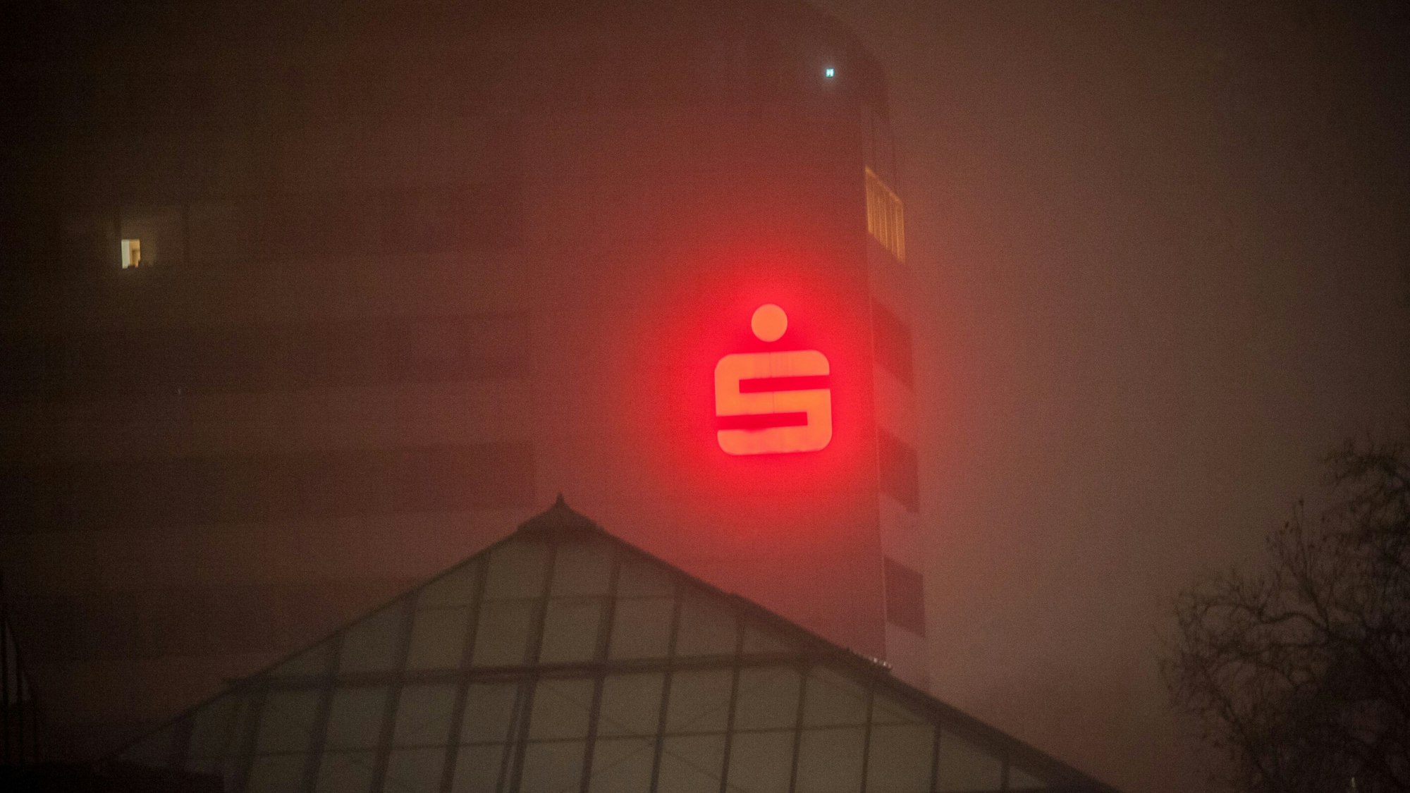 Das rote Logo der Sparkasse Leverkusen an der Fassade des Sparkassen-Gebäudes in Leverkusen-Wiesdorf durchdringt den Nebel.