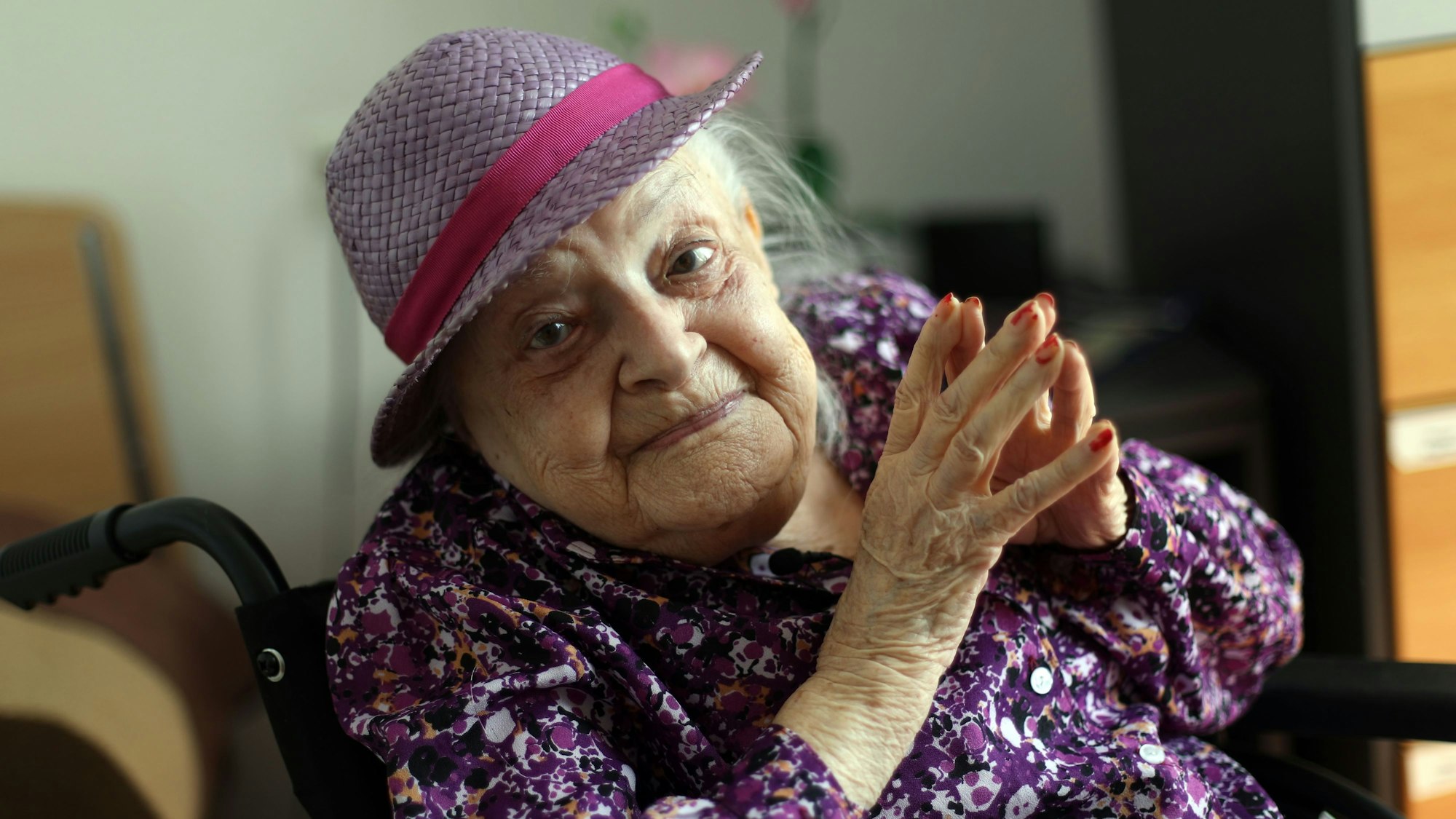 Faye Cukier trägt an ihrem 100. Geburtstag ein lila Hütchen und ein lila Hemd. Sie schaut lächelnd in die Kamera.