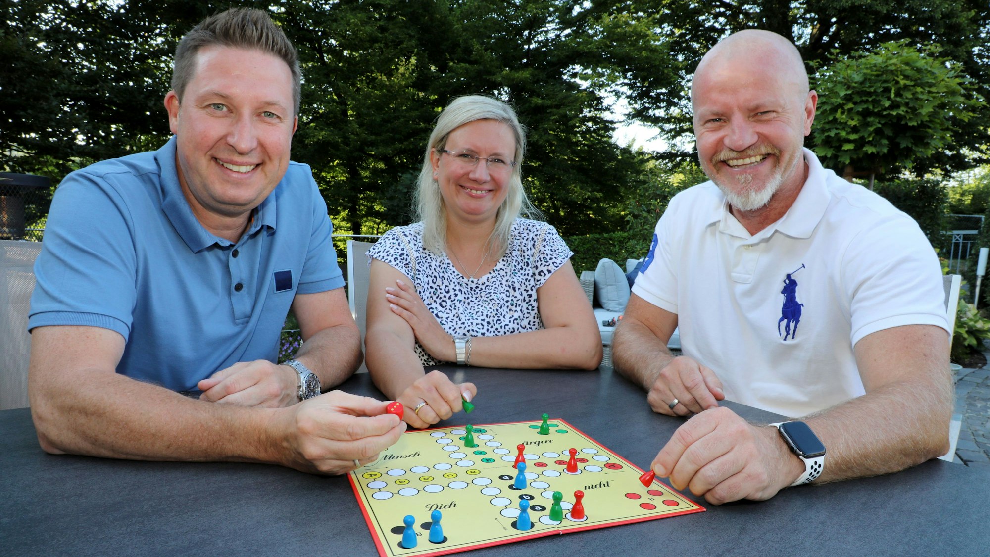 Das Dreigestirn sitzt in zivil an einem Tisch hinter einem Mensch-ärger-dich-nicht-Feld.