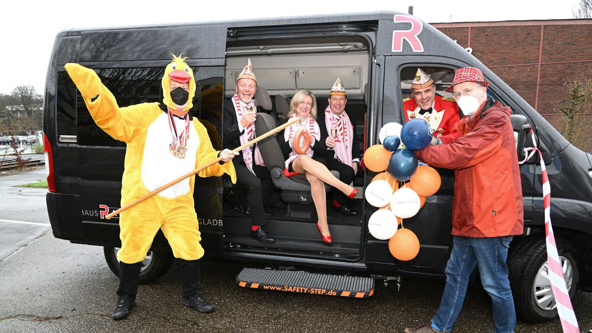 Verkleidete Lokaljournalisten empfangen das Dreigestirn mit Wurst an der Angel in deren schwarzen Transportern.