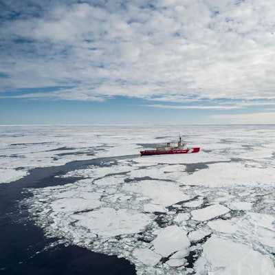 Das rote Schiff der US Küstenwache bricht durch das Packeis der Antatrktis, der Himmel ist bewölkt.