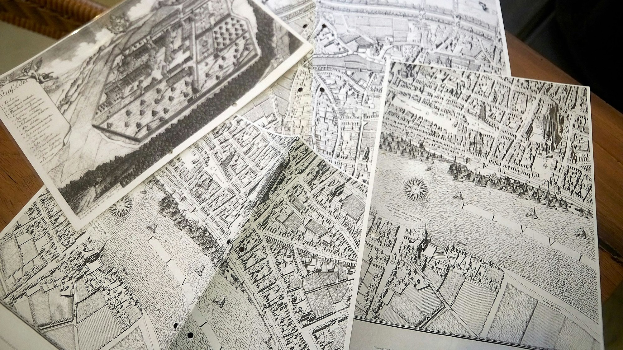 Mehrere alte Stadtpläne von Köln sind auf einem Tisch ausgebreitet.