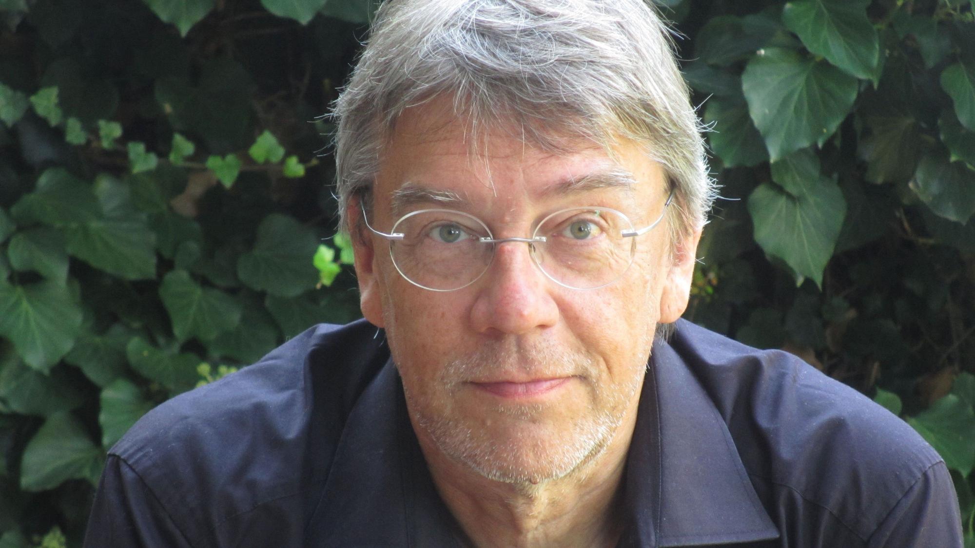 Thilo Winter, Autor von "Der Riss". Er trägt eine Brille und ein schwarzes Hemd. Im Hintergrund sind Blätter eines Busches.