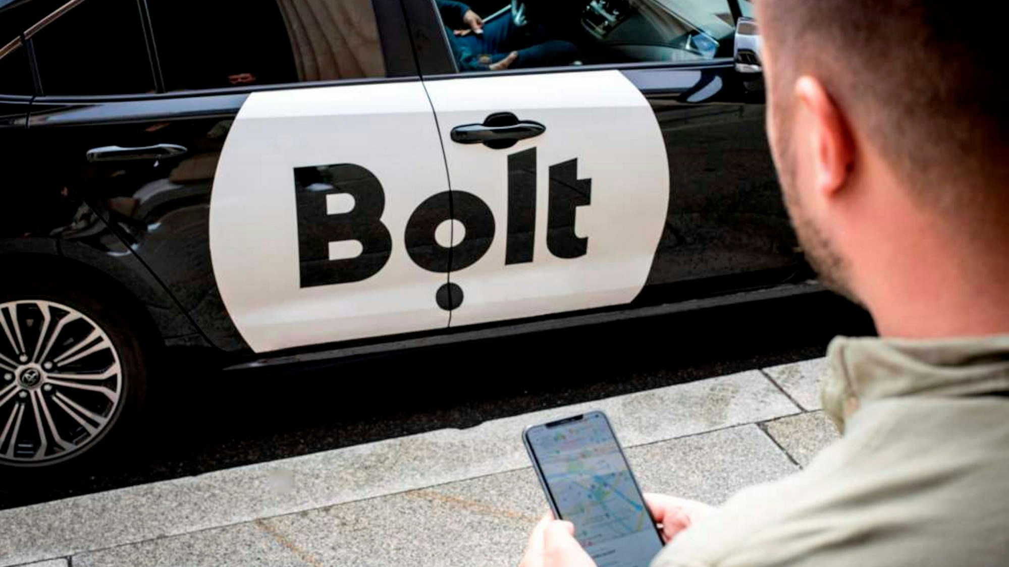Ein Mann mit Smartphone steht vor einem Bolt-Auto