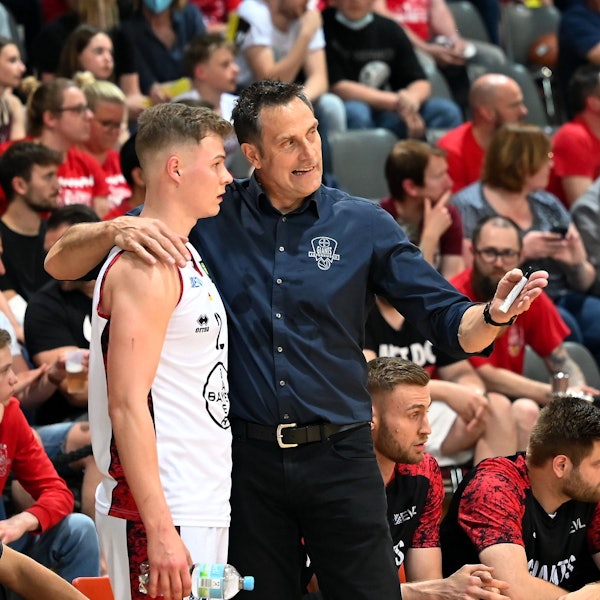 Ein Basketballtrainer legt den Arm um seinen Spieler und erklärt ihm etwas.