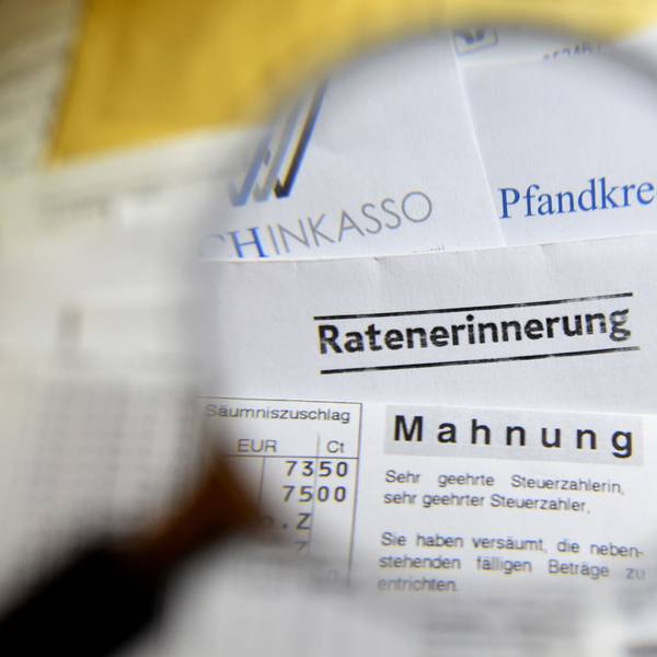 Durch eine Lupe sind Briefe und Dokumente mit Mahnungen, Ratenerinnerung, Pfandkredit, Inkasso und gelbe Briefe vom Gerichtsvollzieher zu sehen.