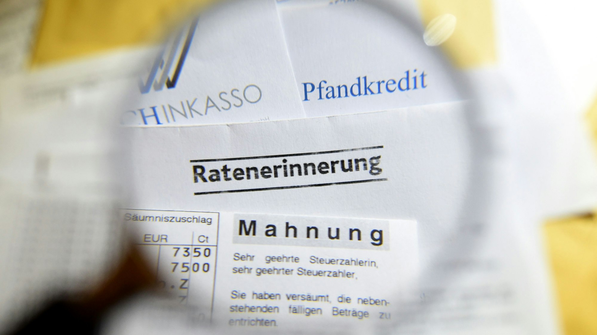 Durch eine Lupe sind Briefe und Dokumente mit Mahnungen, Ratenerinnerung, Pfandkredit, Inkasso und gelbe Briefe vom Gerichtsvollzieher zu sehen.