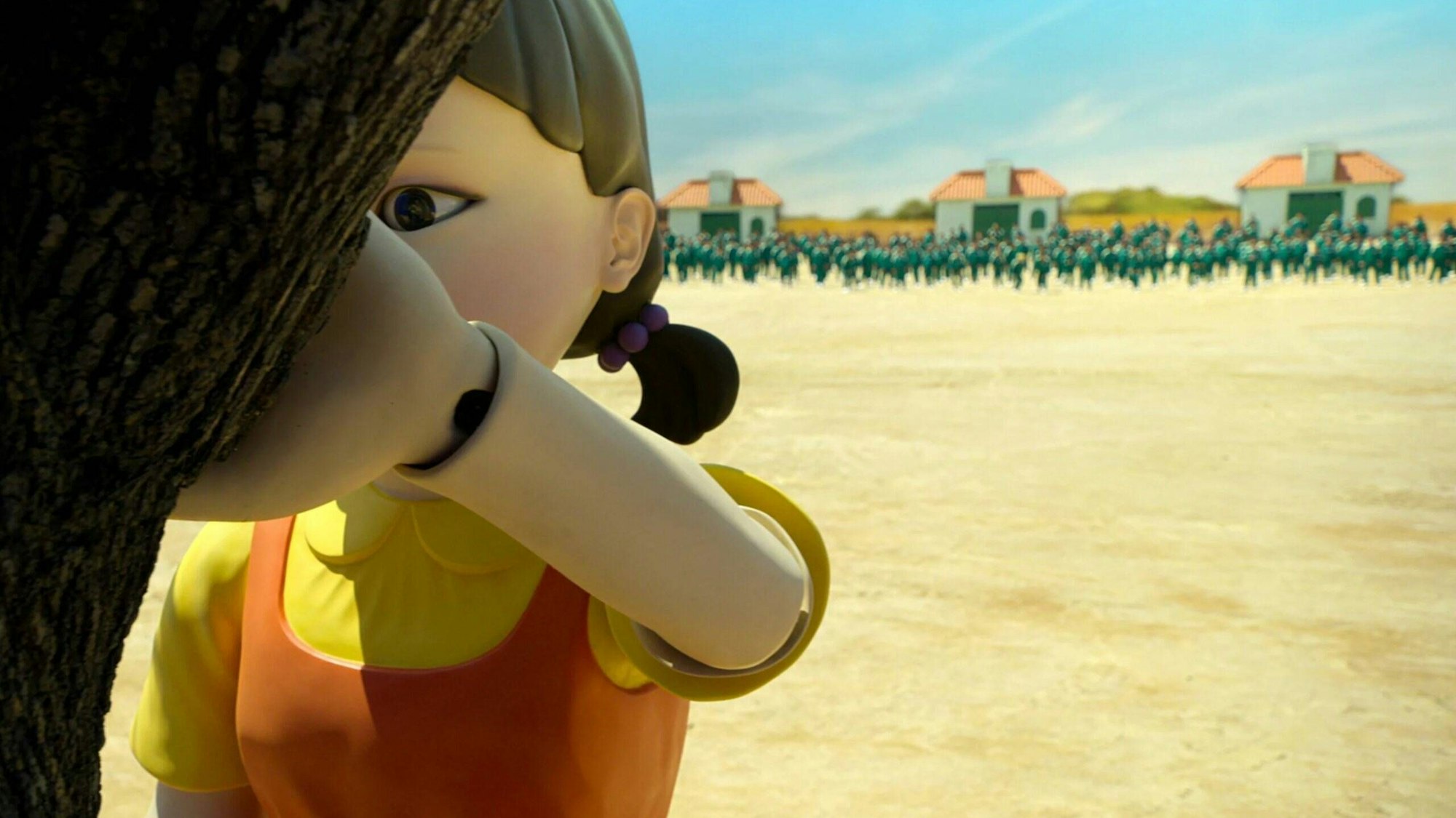 Eine Roboterpuppe lehnt in einer Szene aus der Netflix-Serie „Squid Game“ an einem Baum. Hinter ihr nähern sich die Teilnehmer des Spiels.