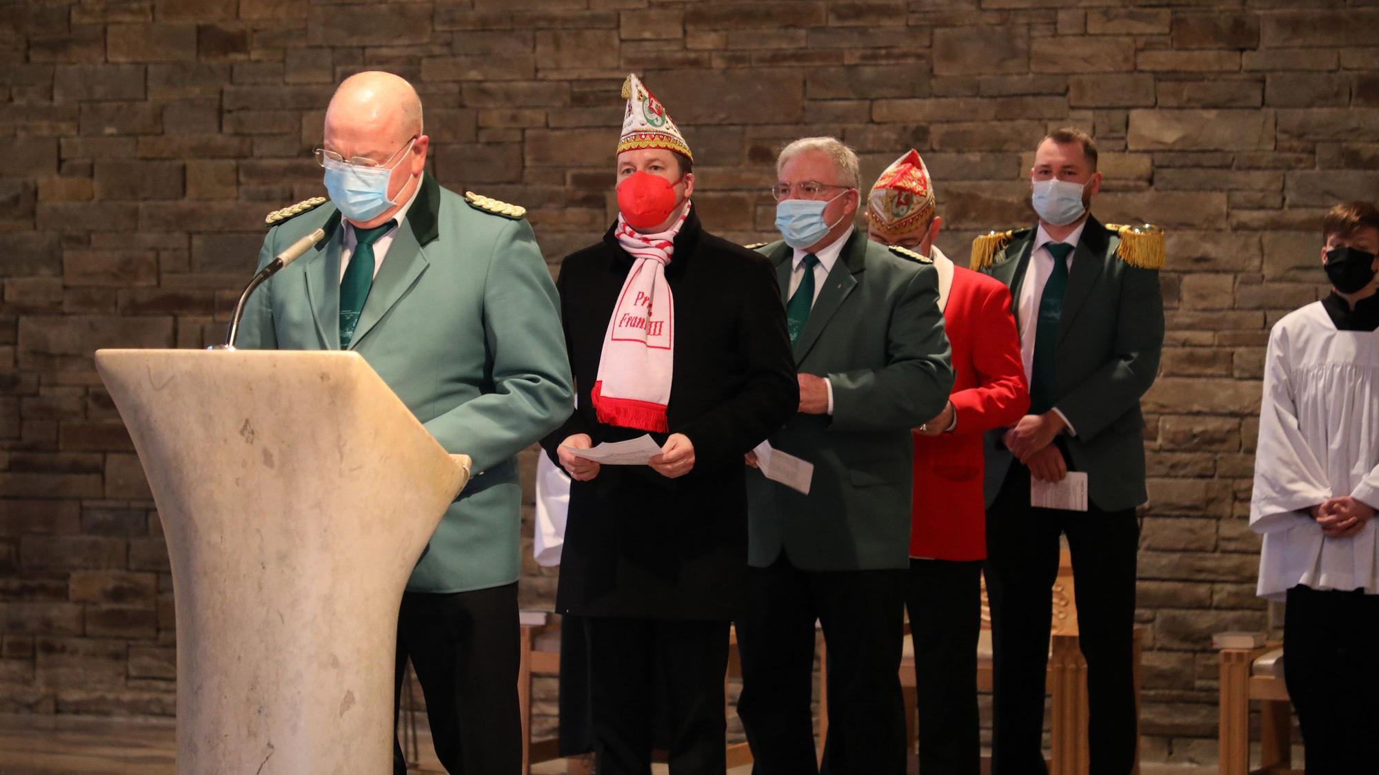 Schützen und Karnevalisten stehen mit FFP2-Maske und Narrenkappe am Ambo in der Kirche.