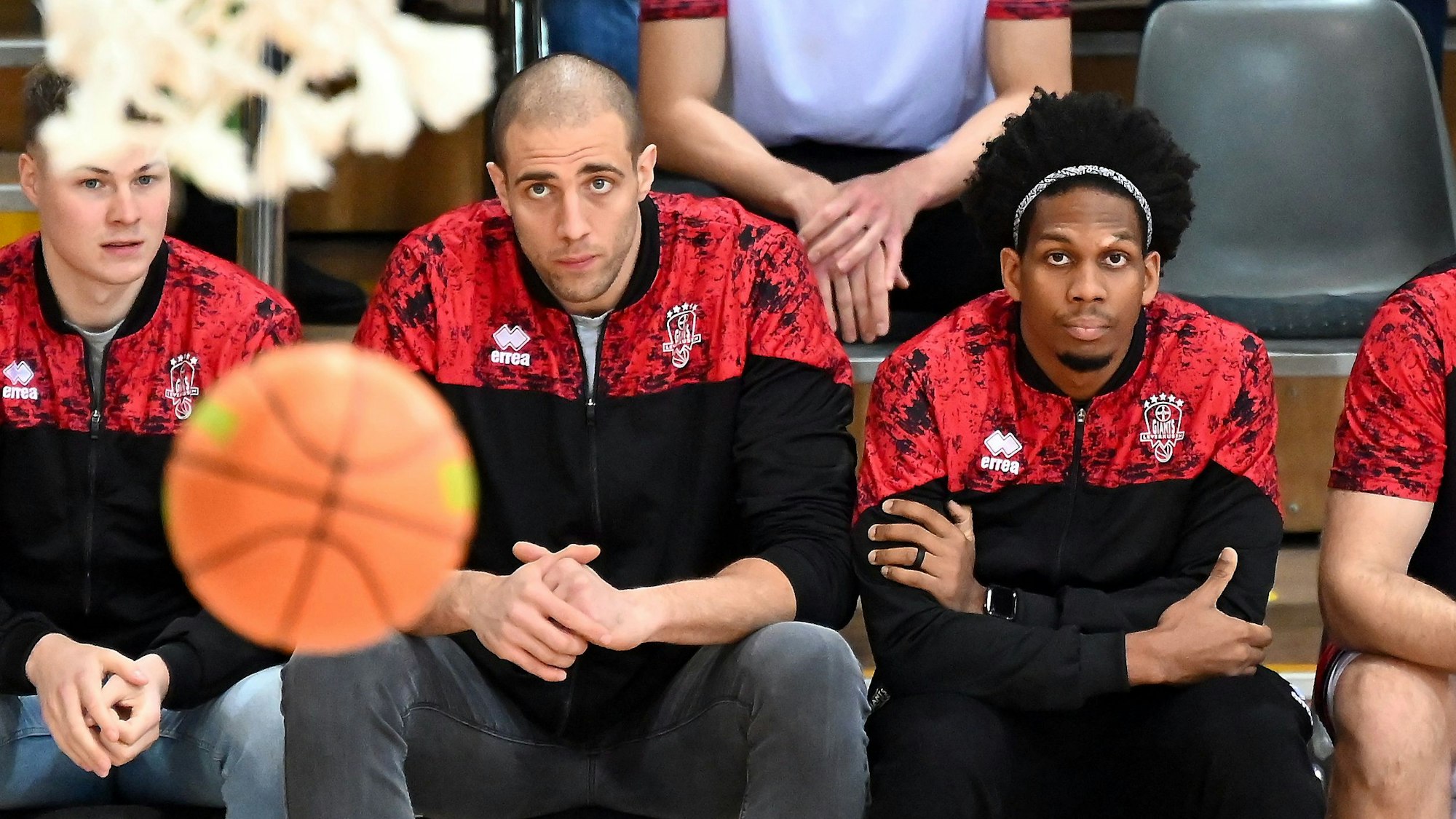 Drei Basketballspieler sitzen auf der Bank und blicken auf den Korb.