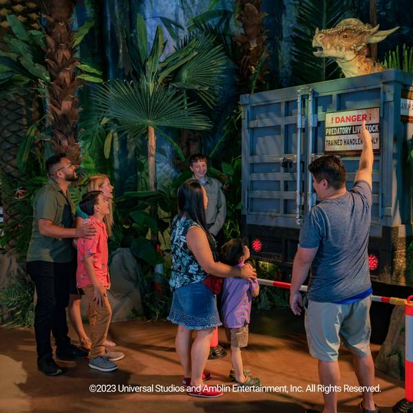 Mehrere Besucher der Jurassic-World-Ausstellung stehen vor einem Modell-Dinosuarier.