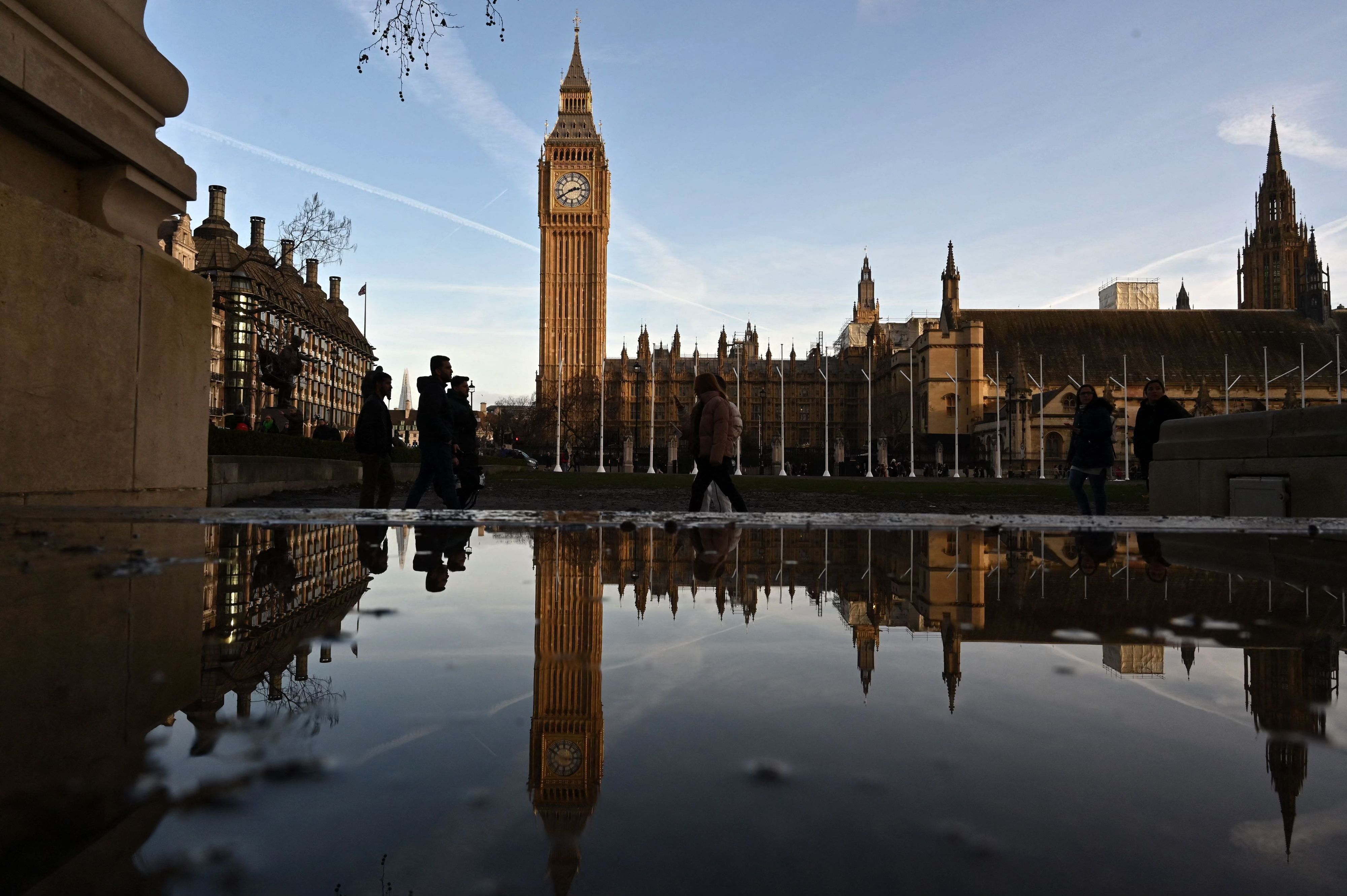 Menschen spazieren vor dem Palace of Westminster in London.