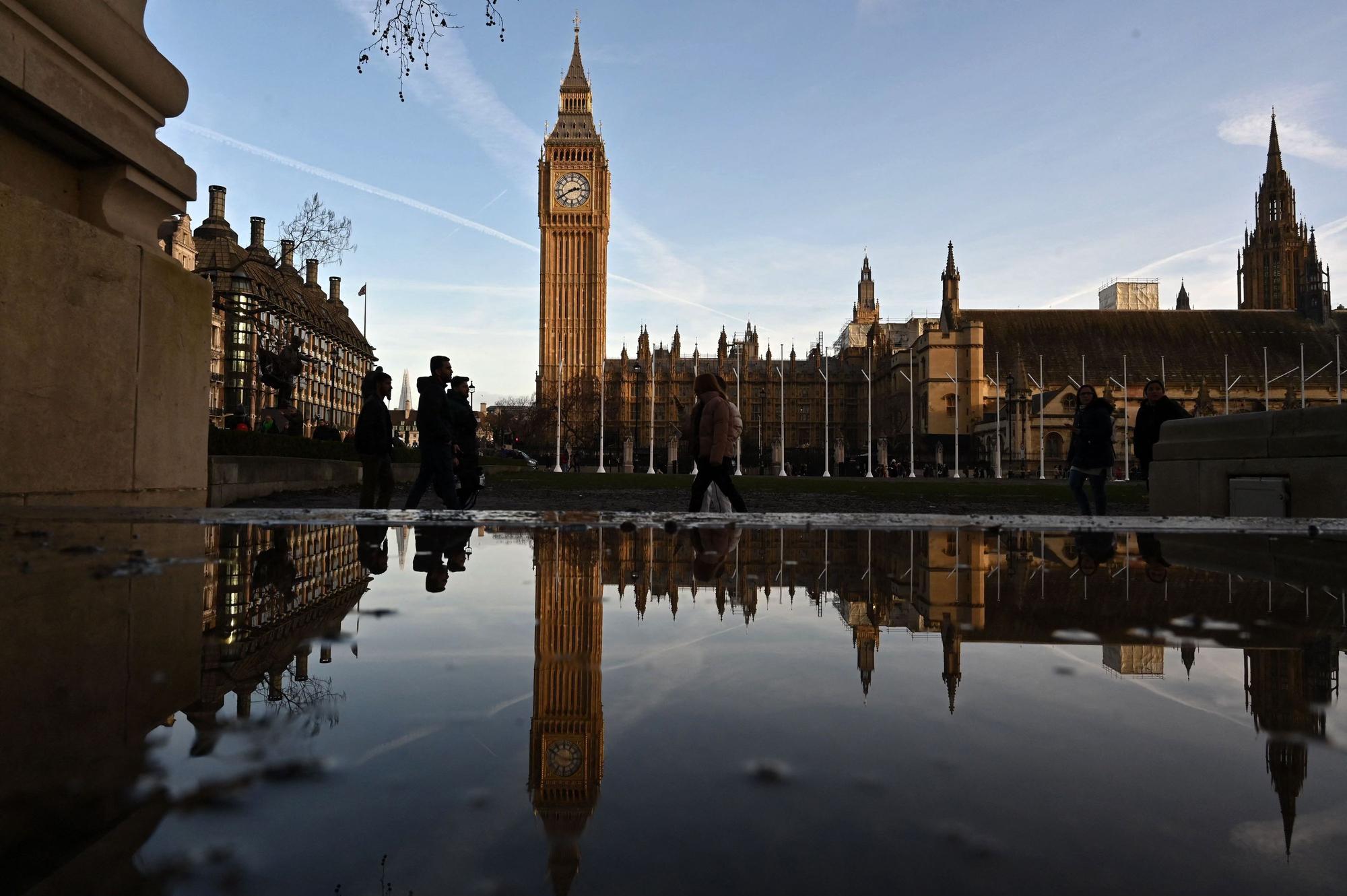 Menschen spazieren vor dem Palace of Westminster in London.