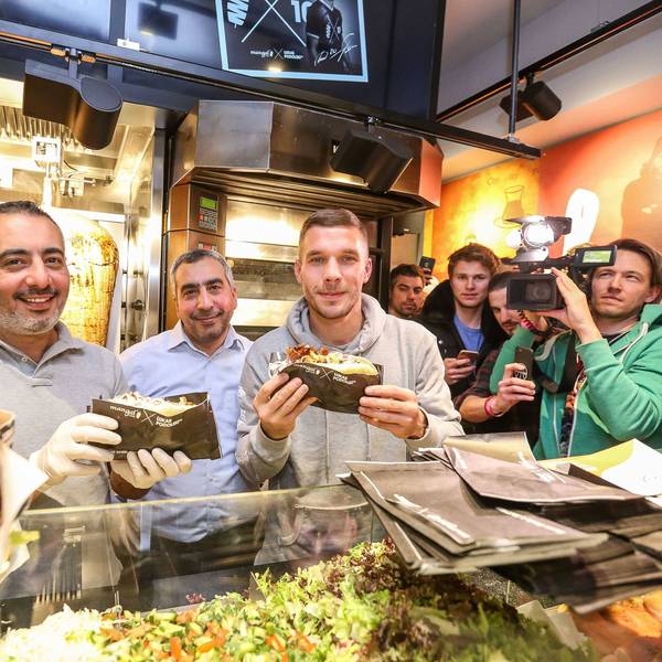 Lukas Podolski posiert mit Kollegen bei der Eröffnung eines Mangal-Döner-Ladens. Die Presse und Fans stehen im Hintergrund.
