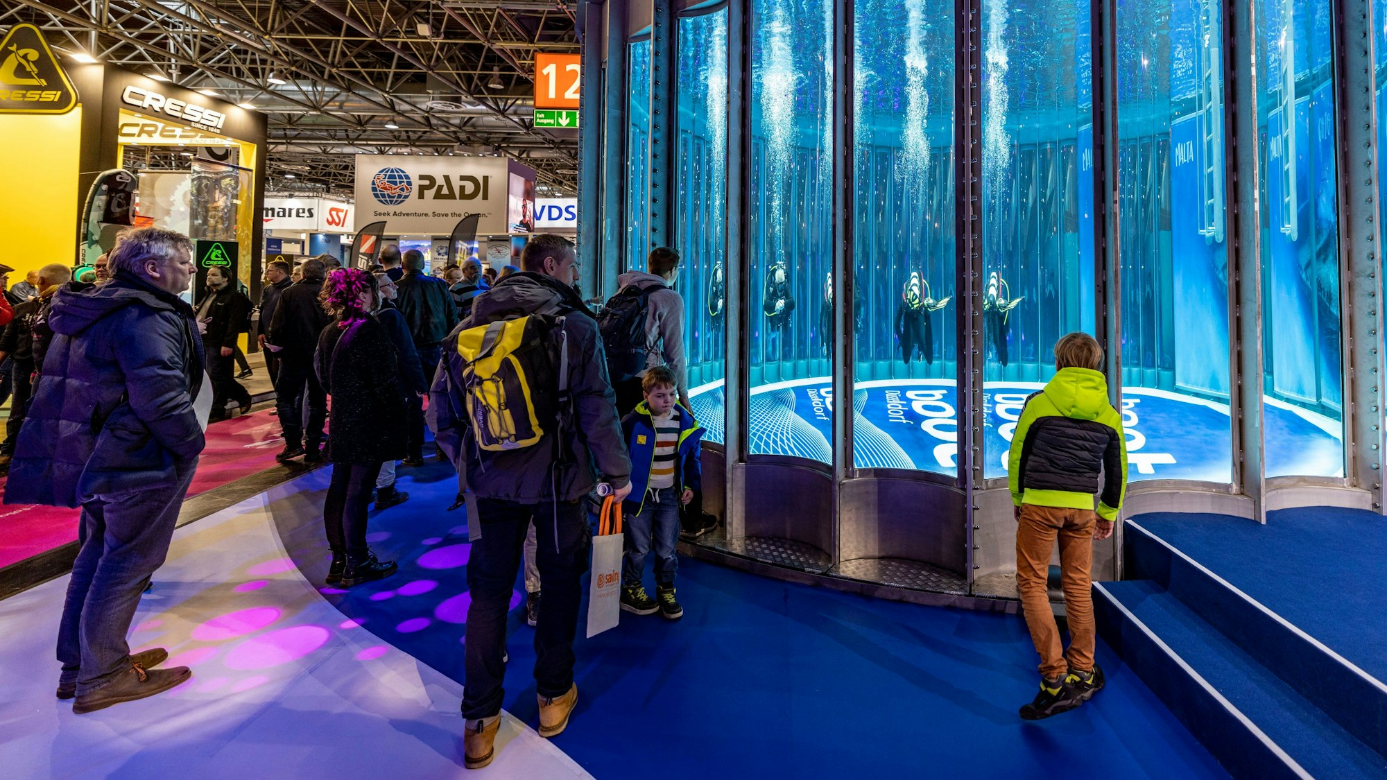 Taucher drehen in einer Messehalle in einem Tauchturm mit Rund-Um-Sicht ihre Runden.