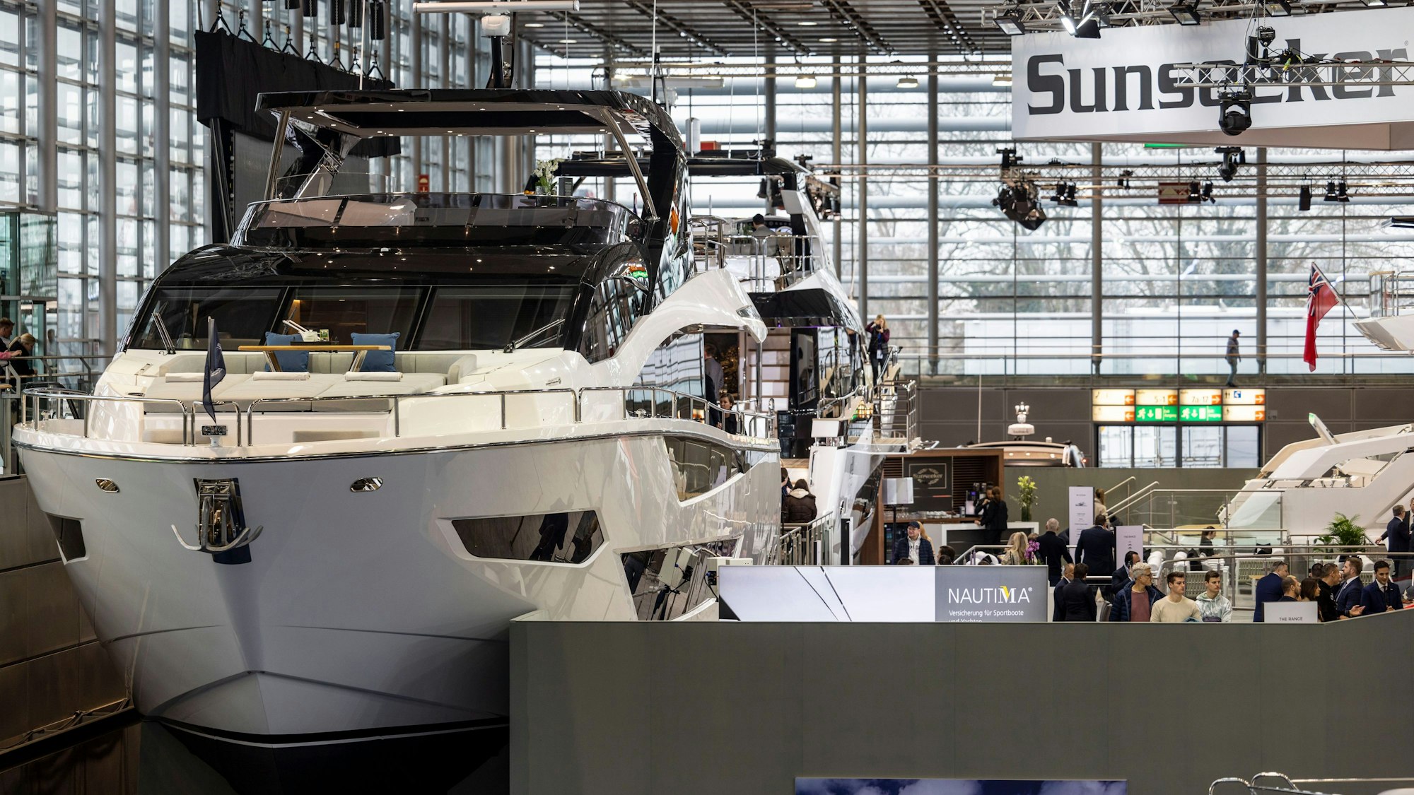 Besucher schauen sich teure Jachten in einer Messehalle an.