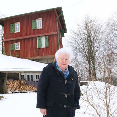 Eine Frau steht vor dem verschneiten Blockhaus aus Holz.