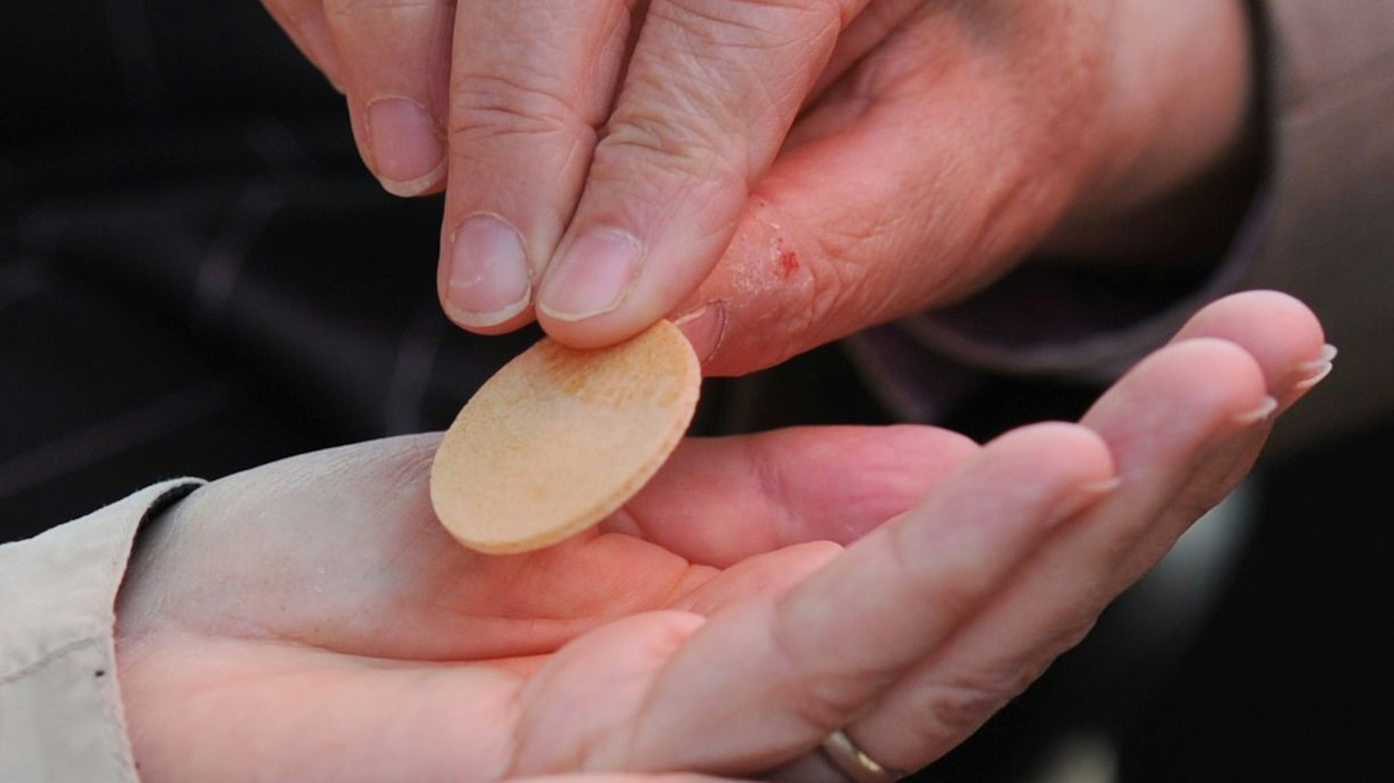 Eine Hand legt eine Hostie in die eine andere Hand.