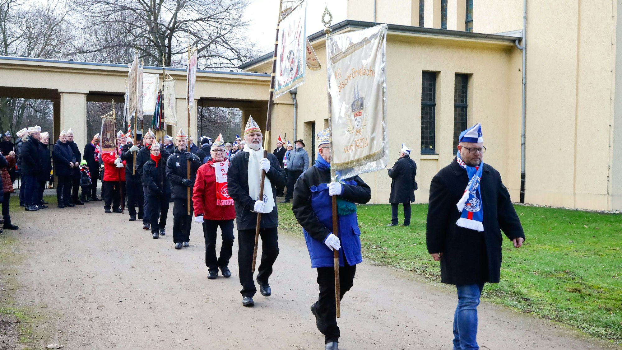 Kölner Karnevalsvereine laufen der Reihe nach mit ihren Karnevalsfahnen auf den Jüdischen Friedhof in Köln-Bocklemünd.