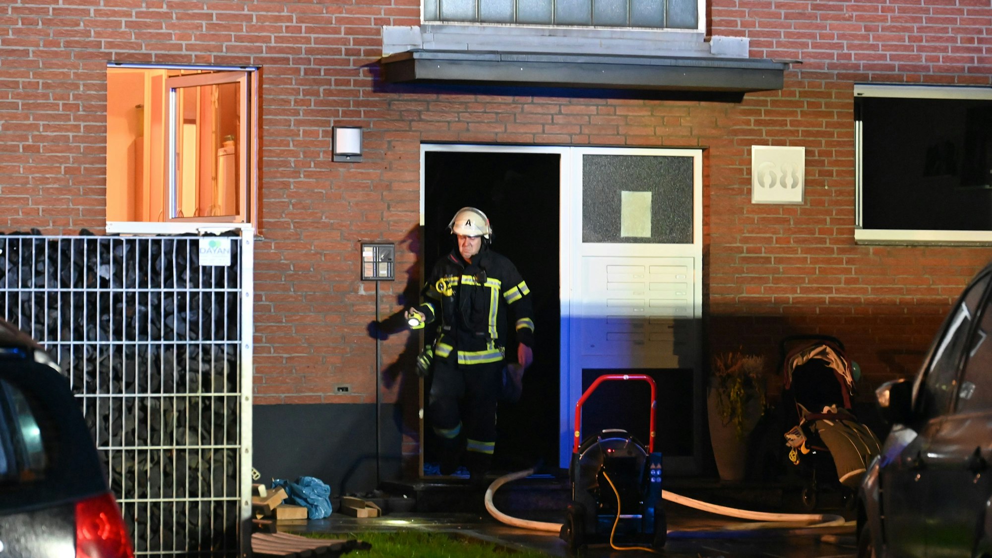 Ein Feuerwehrmann kommt aus einer Haustür. Ein Fenster im Erdgeschoss steht weit offen.