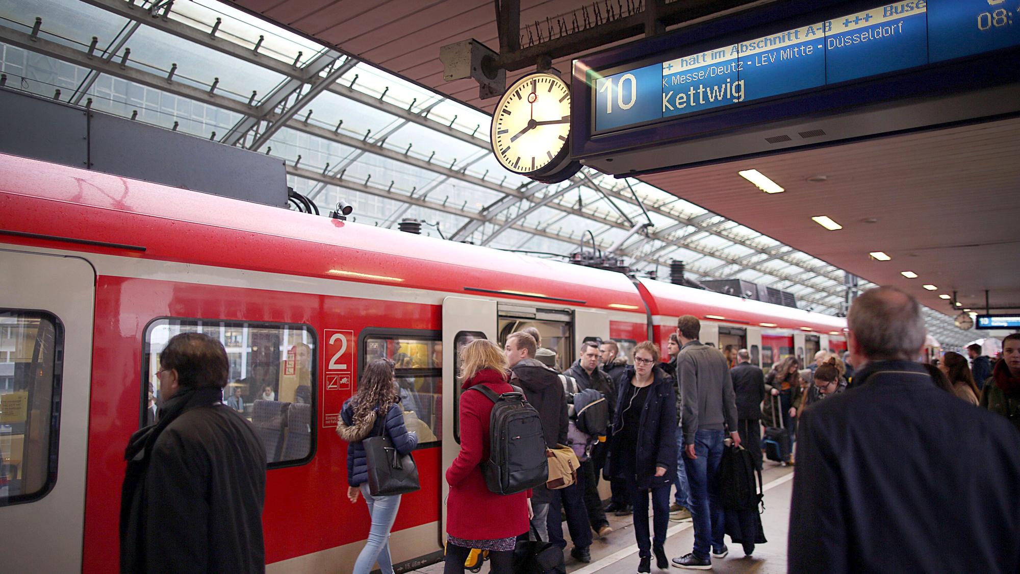 Pendler stehen im Hauptbahnhof Köln vor einer S-Bahn.