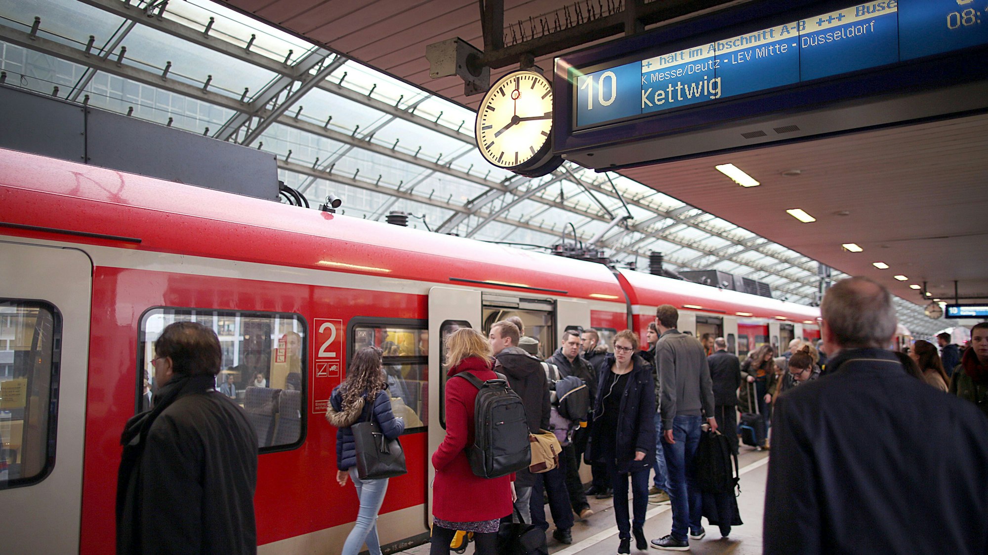 Pendler stehen im Hauptbahnhof Köln vor einer S-Bahn.