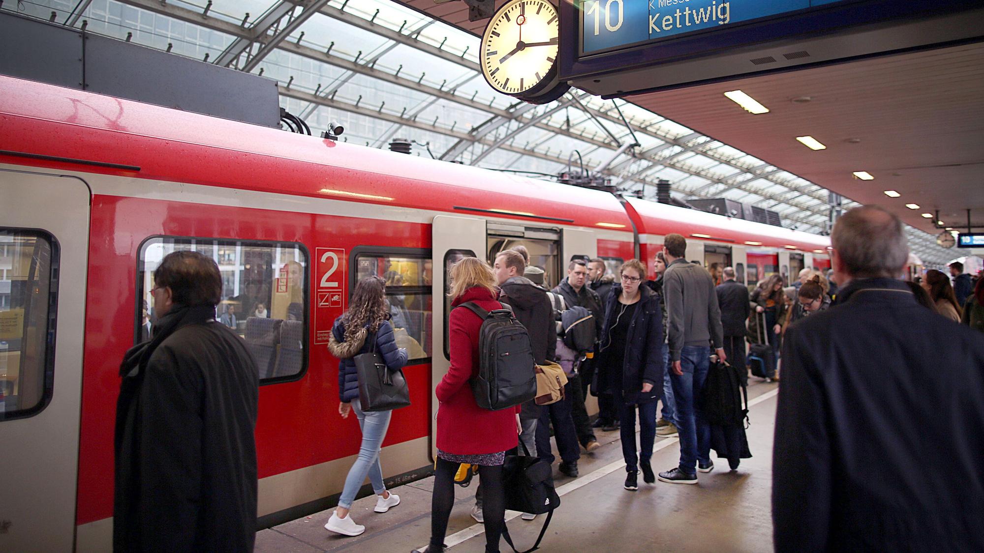 Pendler stehen im Hauptbahnhof Köln vor einer S-Bahn.