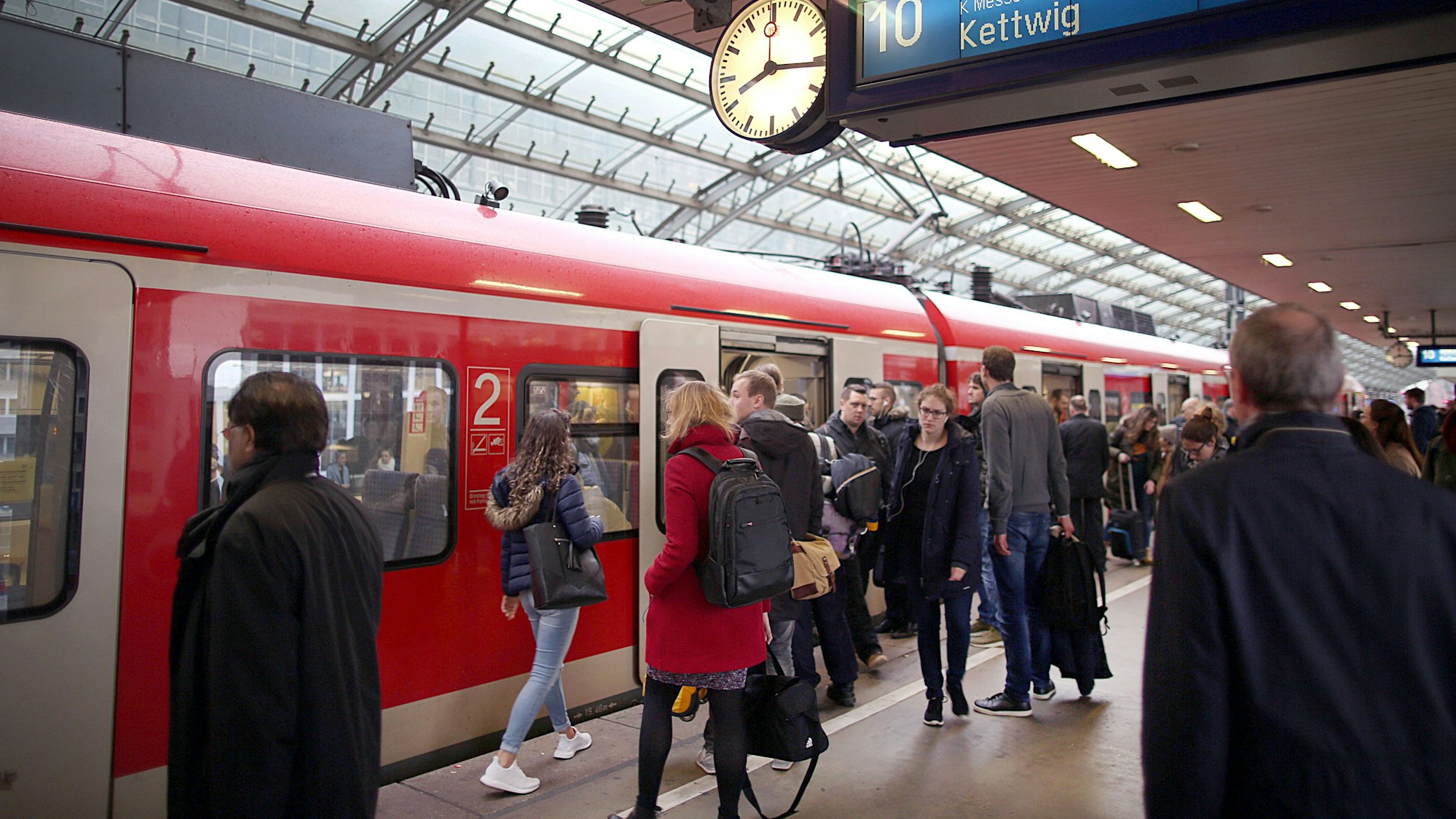 Pendler stehen im Hauptbahnhof Köln vor einer S-Bahn.