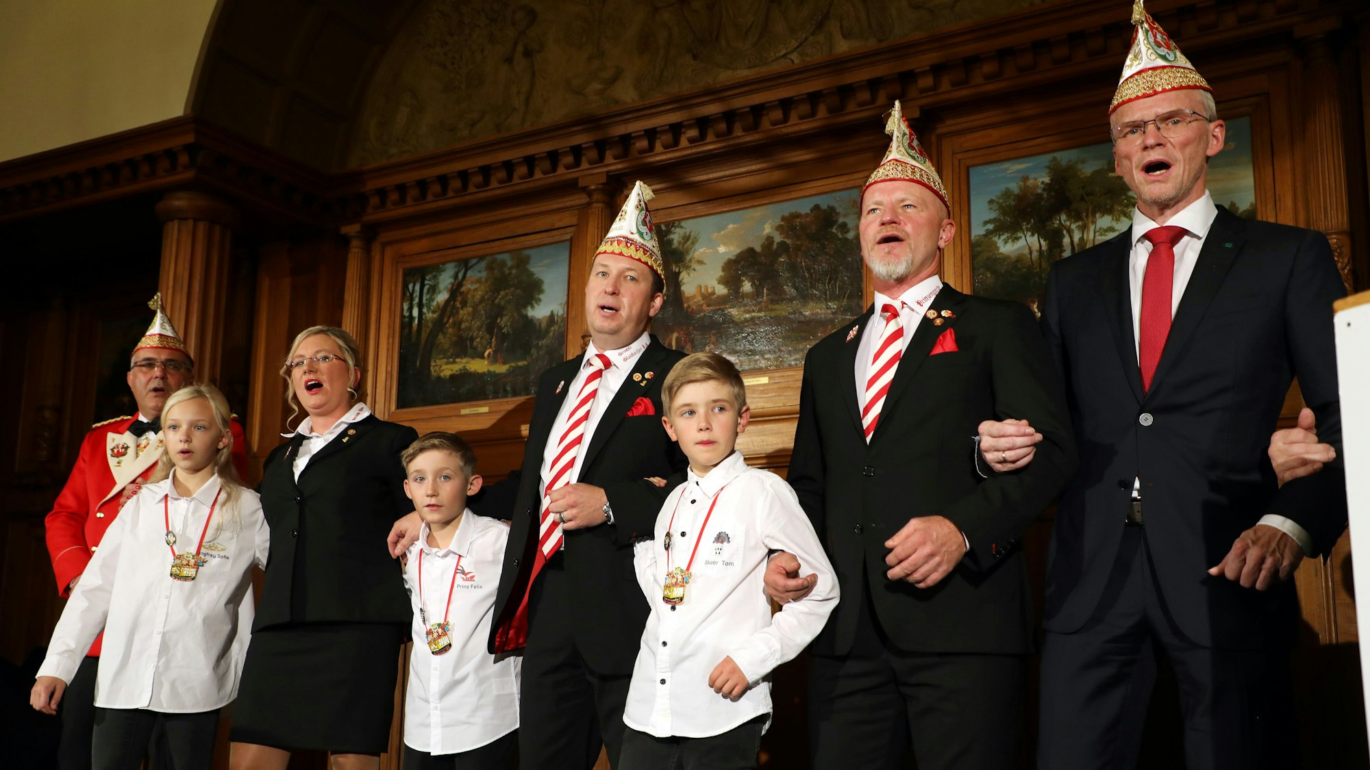 Das Dreigestirn Prinz in spe steht schunkelnd und singend in Anzügen auf der Bühne.