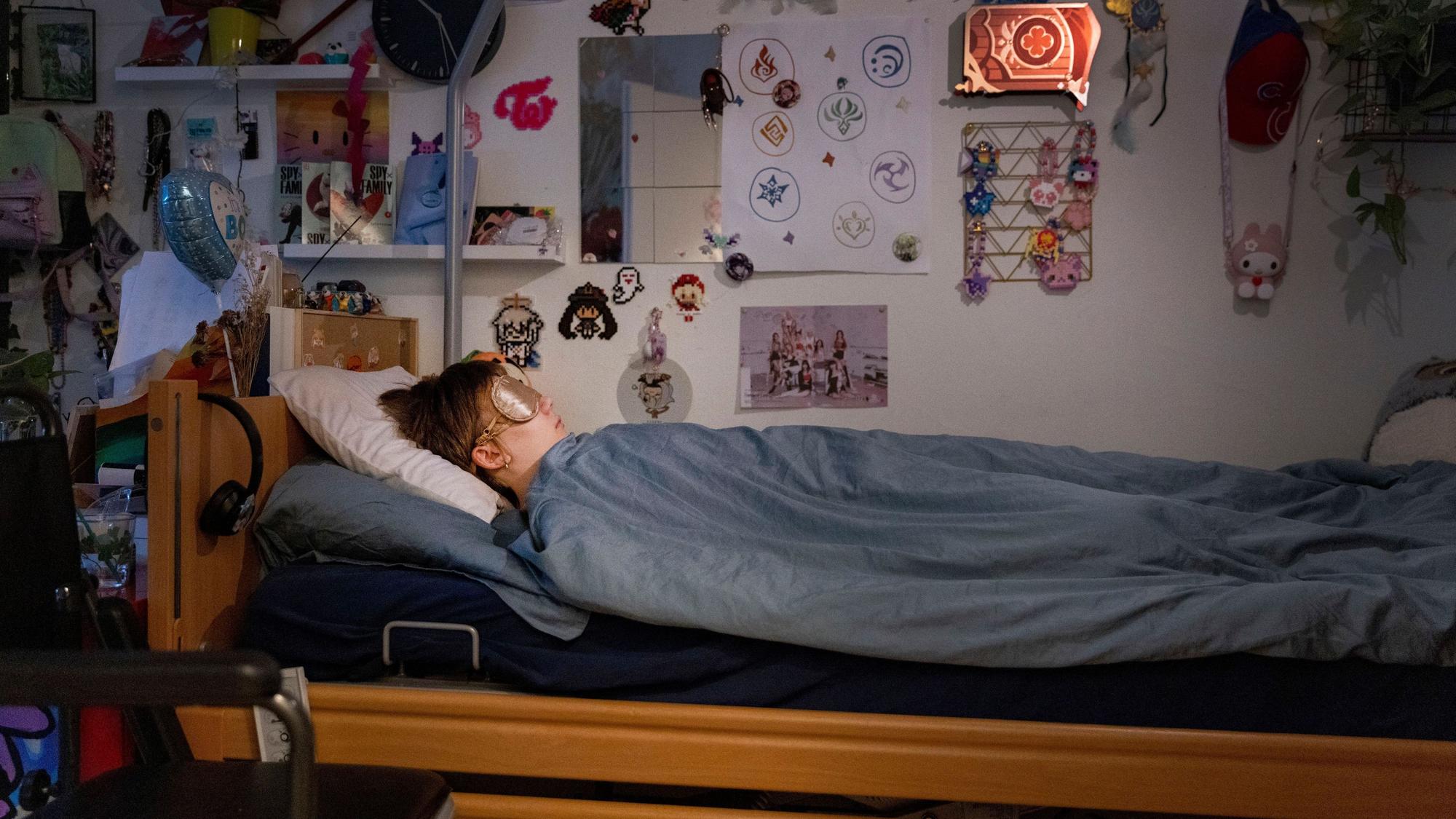 Ed liegt in seinem Bett, er trägt eine Schlafmaske. Vor dem Bett steht ein Rollstuhl. An den Wänden kleben unzählige Bilder, Zeichnungen und Figuren.