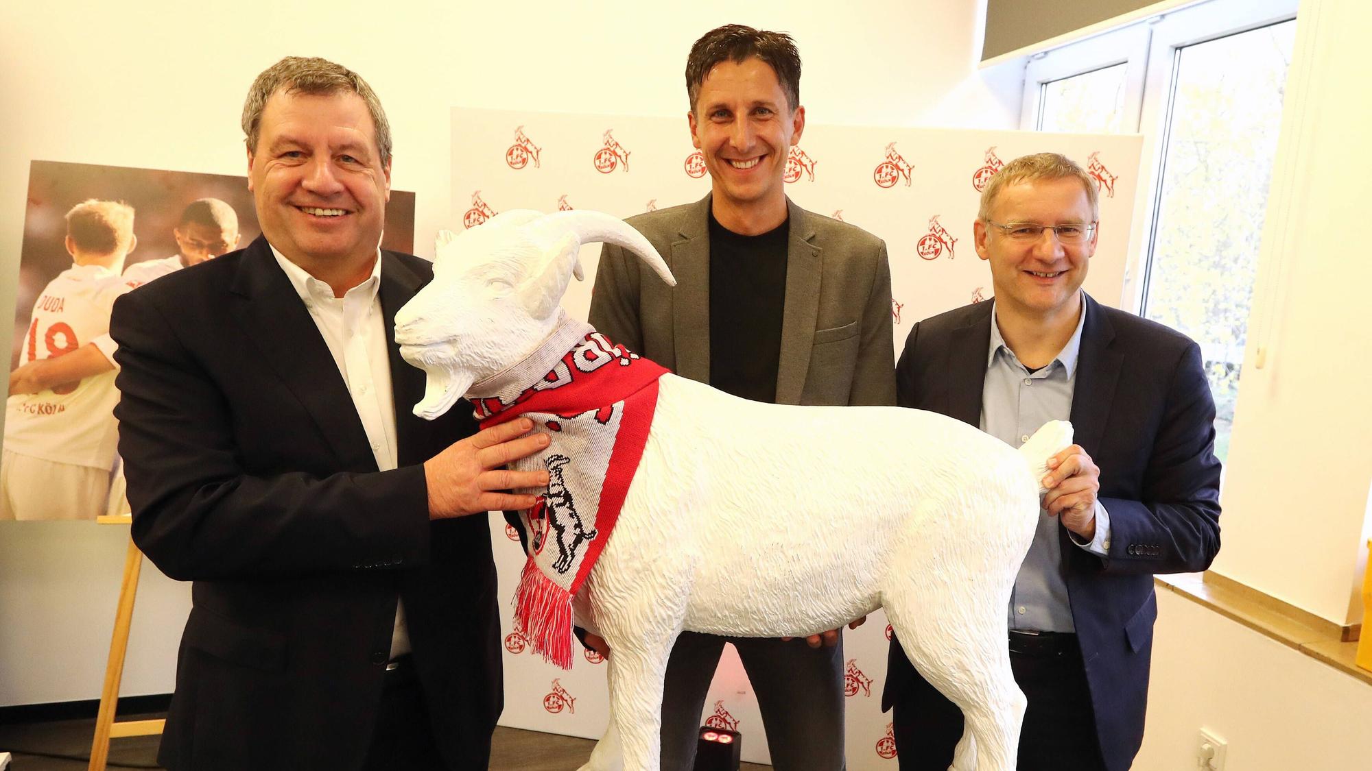 Präsident Werner Wolf und sein Vize Eckhard Sauren bei der Präsentation des Kölner Geschäftsführers Christian Keller. Die drei Herren halten gemeinsam einen Abguss des Kölner Geißbocks Hennes und lachen in die Kamera.