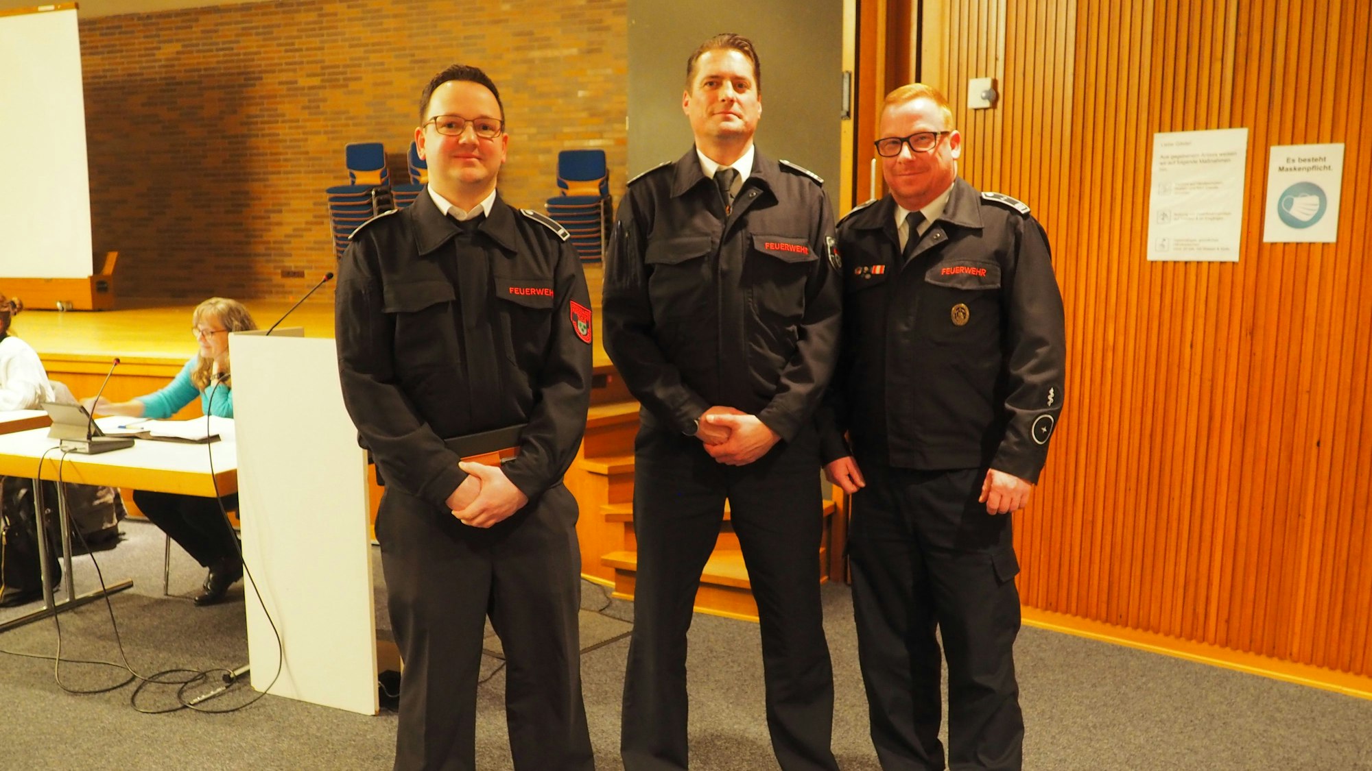 Drei Feuerwehrmänner stehen im dunklen Dienstanzug in aufrechter Haltung im Ratssaal im Haus der Kunst.