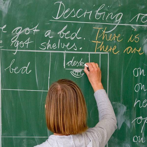 Eine Lehrerin einer Grundschule schreibt in englischer Sprache an die Tafel.