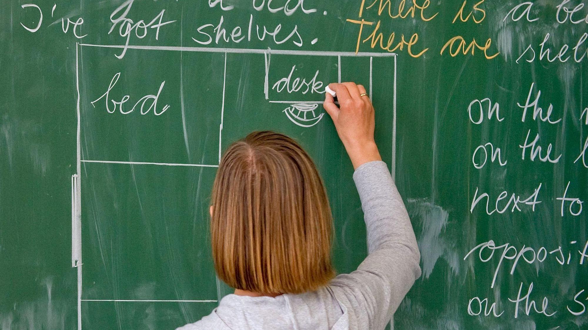 Eine Lehrerin einer Grundschule schreibt in englischer Sprache an die Tafel.