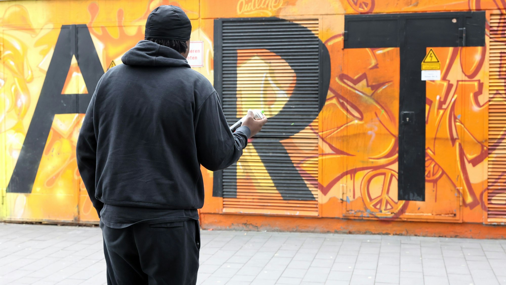 Chris steht mit dem Rücken zur Kamera vor einer mit Grafitti besprühten Mauer.