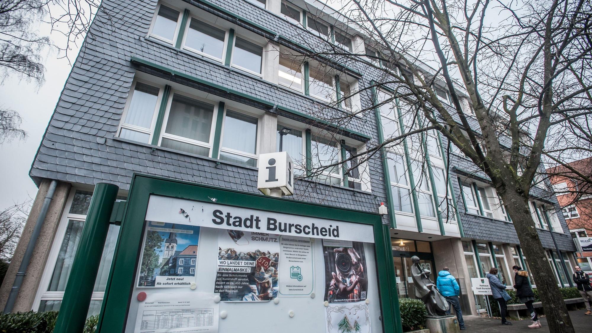 Eine grün gerahmte Info-Vitrine mit der Aufschrift „Stadt Burscheid“ vor dem verschieferten Rathaus der Stadt.